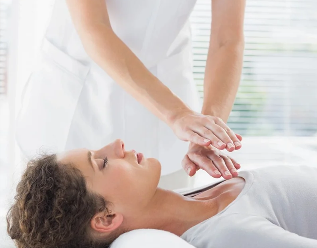 Mujer recostada con los ojos cerrados mientras otra persona coloca sus manos sobre su pecho en una sesión de terapia energética.